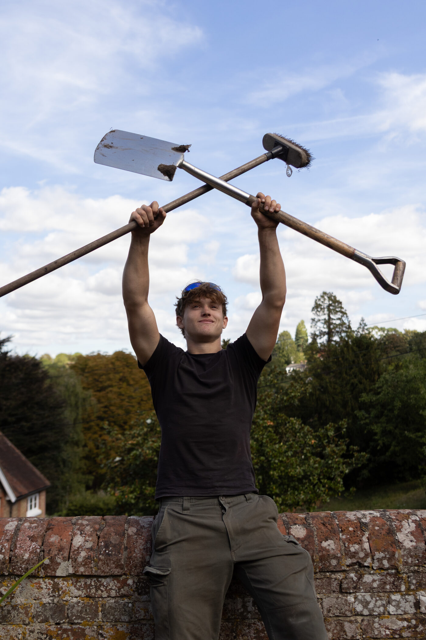 Austin on a garden wall with a spade and a broom